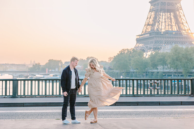 Man and woman holding hands near the Eiffel Tower at Bir-Hakeim Bridge during a romantic Paris couples photoshoot, with the woman wearing a dress.