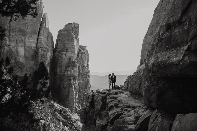 black and white photo of a couple standing at the top of cathedral rock during sunset in fancy clothes
