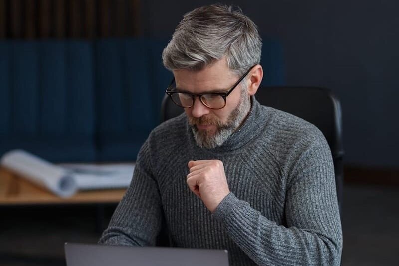 stressed man in gray looks at laptop