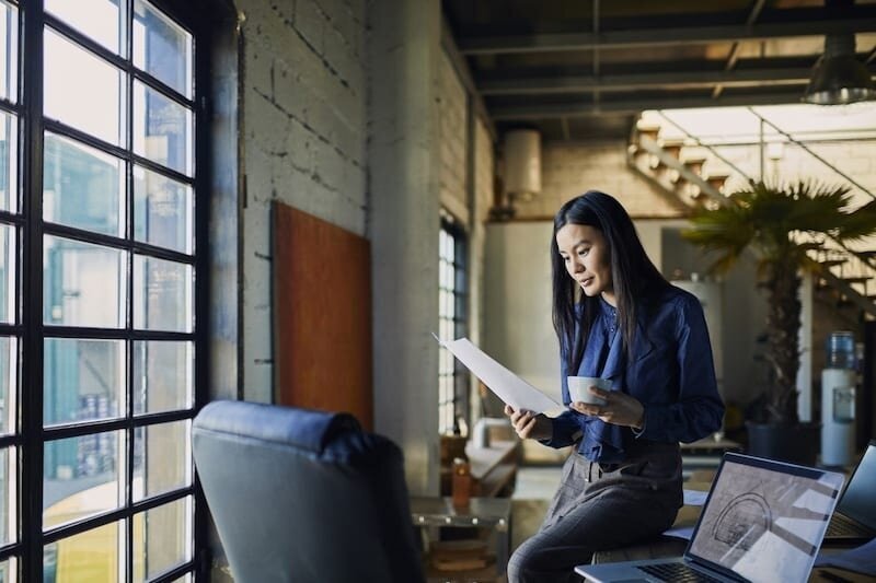 asian architect leans on her desk and reviews papers