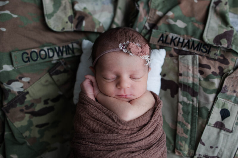 Newborn baby girl wrapped in a brown blanket and sleeping in between her parents army turn outs