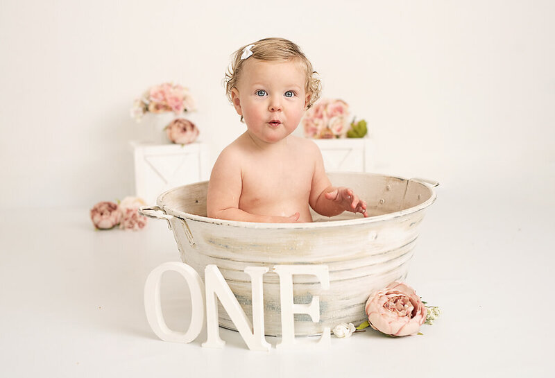 Baby girl in vintage bathtub with pink flowers on first birthday