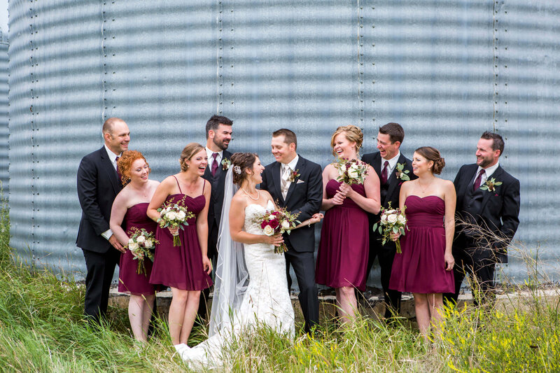large wedding party laughing in front of grain bin