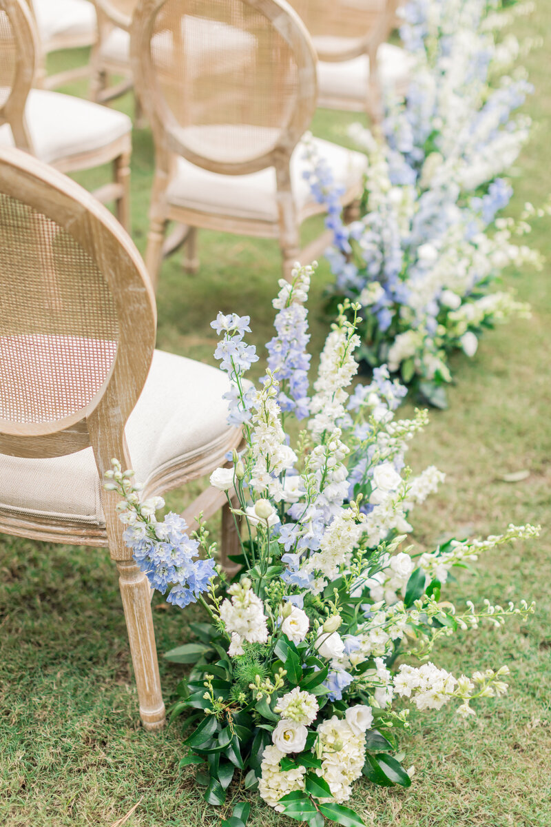 Elegant wooden chairs adorned with lush white and blue floral arrangements, creating a dreamy ceremony aisle setting