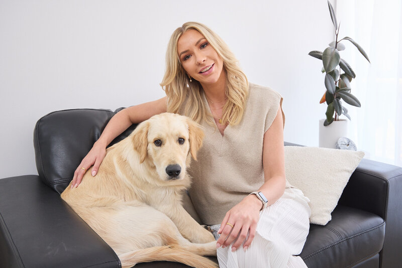 Woman sitting on a couch with a dog by her side. The woman appears to be indoors, and the setting suggests a cozy and comfortable environment.