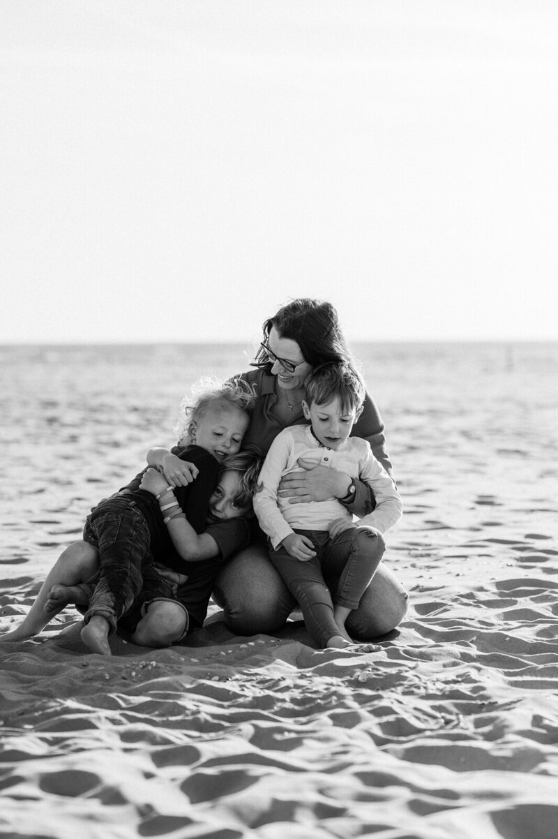 Moeder zit met haar drie zoons op schoot op het strand te stoeien