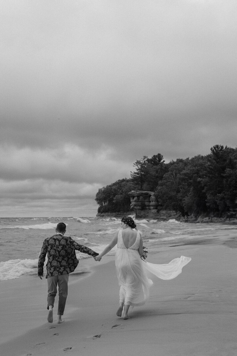 couple running on the beach holding hands dressed in wedding attire