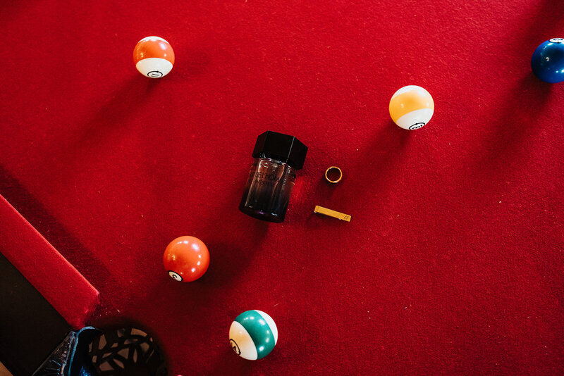 groom cologne ring and tie clip scattered on a pool table with pool balls 