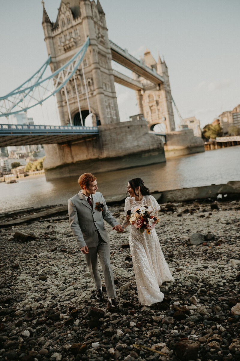Bride and groom on the shore of the Thames in front of Tower Bridge in London on their wedding day. 
