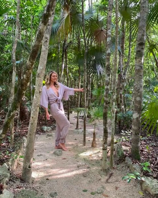Sheldan Paige, barefoot and serene in a soft lavender robe, walking a sacred jungle path in Tulum where she offers life coaching and holistic healing sessions immersed in nature.