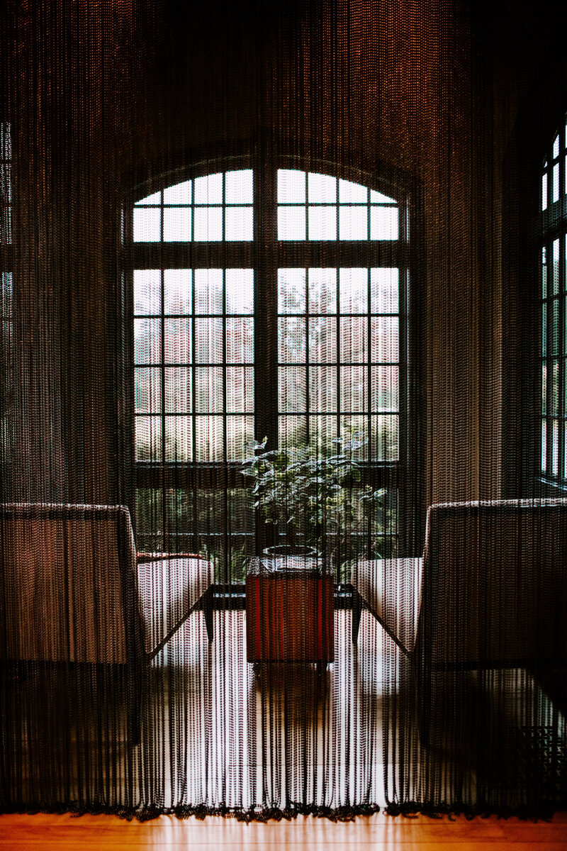 Sheer black curtain hangs in front of a room with two lounge chairs sitting in front of a large arched window | Interior photography by Sara Coffin Photo in NC
