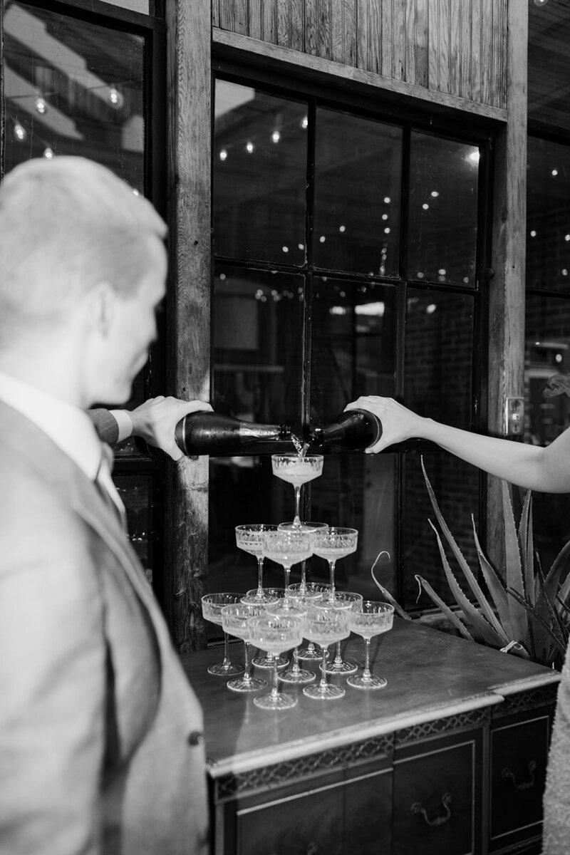 Black and white image of bride and groom pouring champagne in stack of glasses