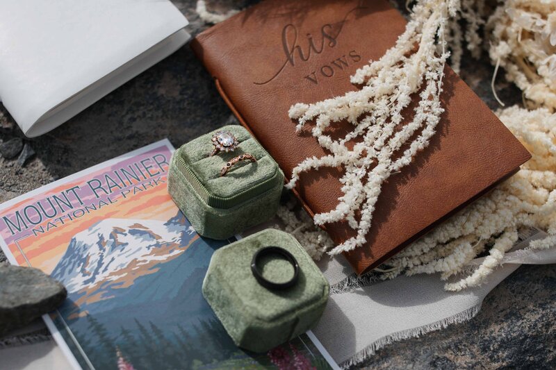 close up detail shot of wedding rings, a vow book, and a Mount Rainier post card