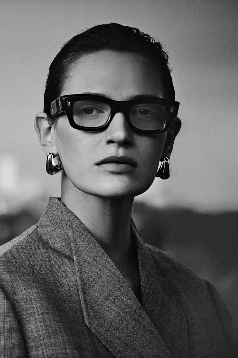 Close-up black and white shot of a woman with a grey blazer wearing thick rimmed Cutler and Gross glasses.