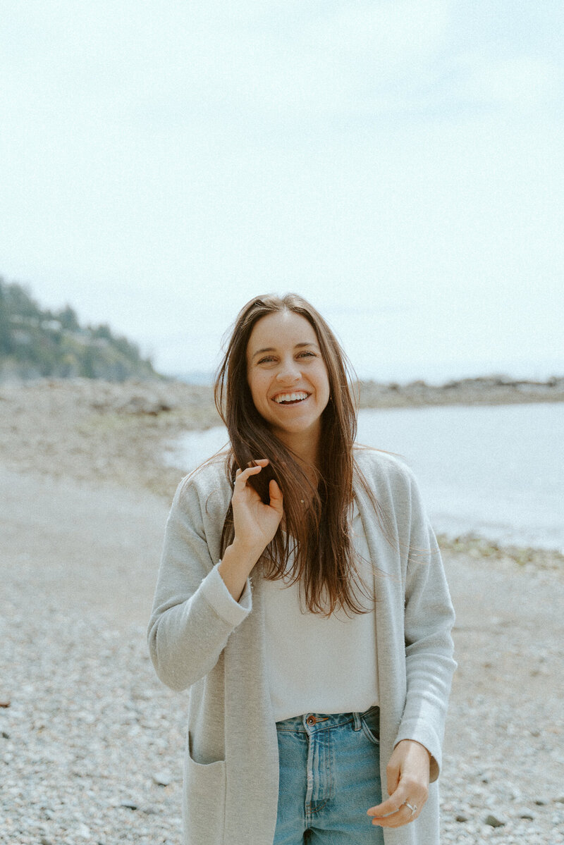 Woman with brown curled hair wearing a beige sweater holds two halves of an avocado