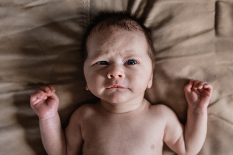 Newborn baby boy laying on bed looking up by newborn photographer Lisa Smith Photography