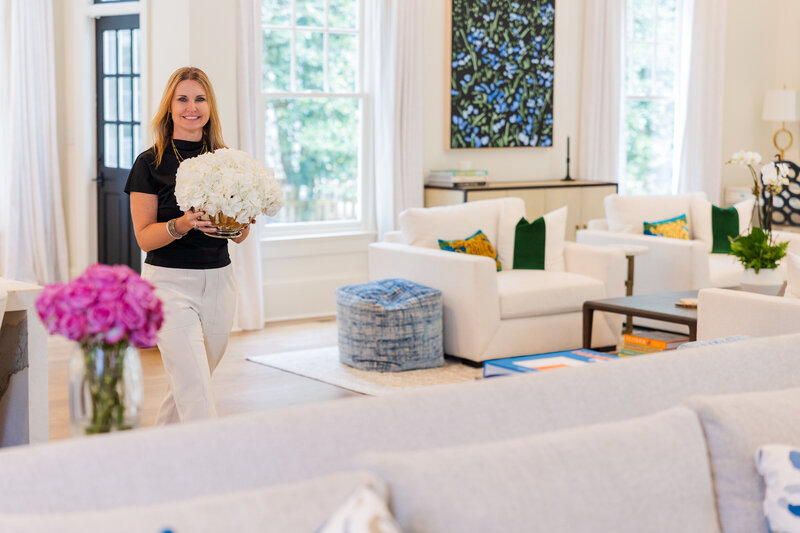 realtor woman wearing a black and white outfit walking into a living room holding a vase of flowers during Atlanta branding photoshoot