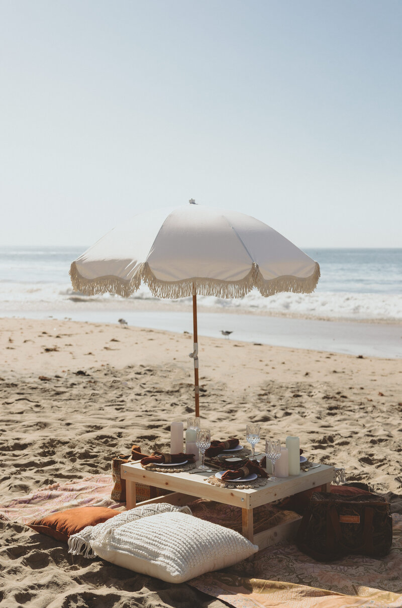 Let's Picnic Co. - Picnic table and umbrella with warm  orange decor on the beach in Corona Del Mar California