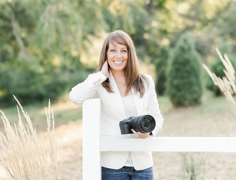 Jennifer Hall, who is the lead photographer at Jennifer Hall Photography, LLC, stands next to a fence.