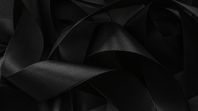 Black shiny fabric with deep folds and soft sheen, creating a moody, elegant backdrop.