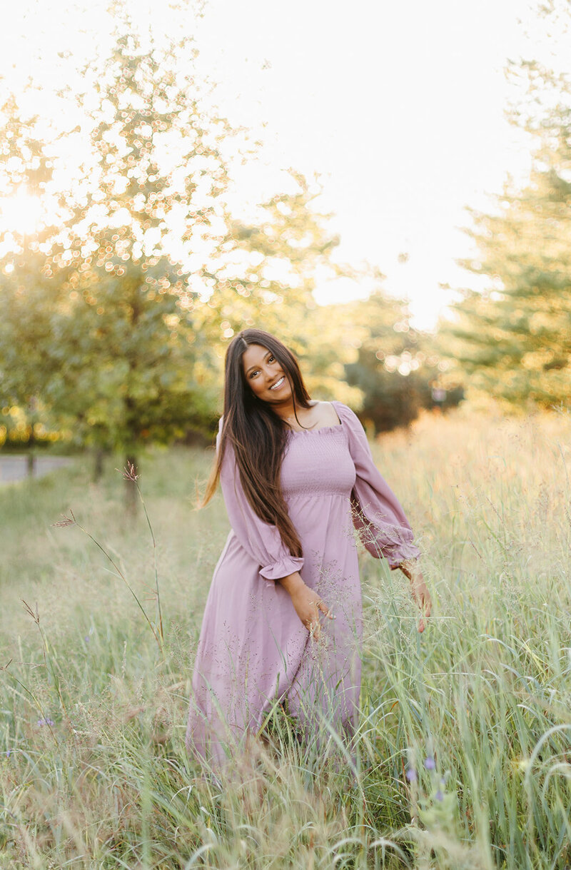 Senior girl in a pink dress posing in a grassy field