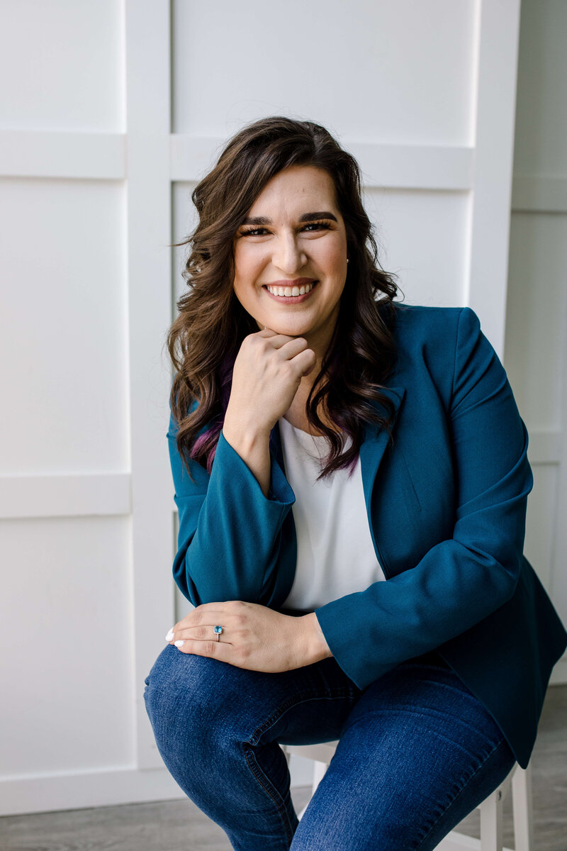 brand photography for small business owners with portrait style headshot with woman in a dark blue blazer sitting on a stool
