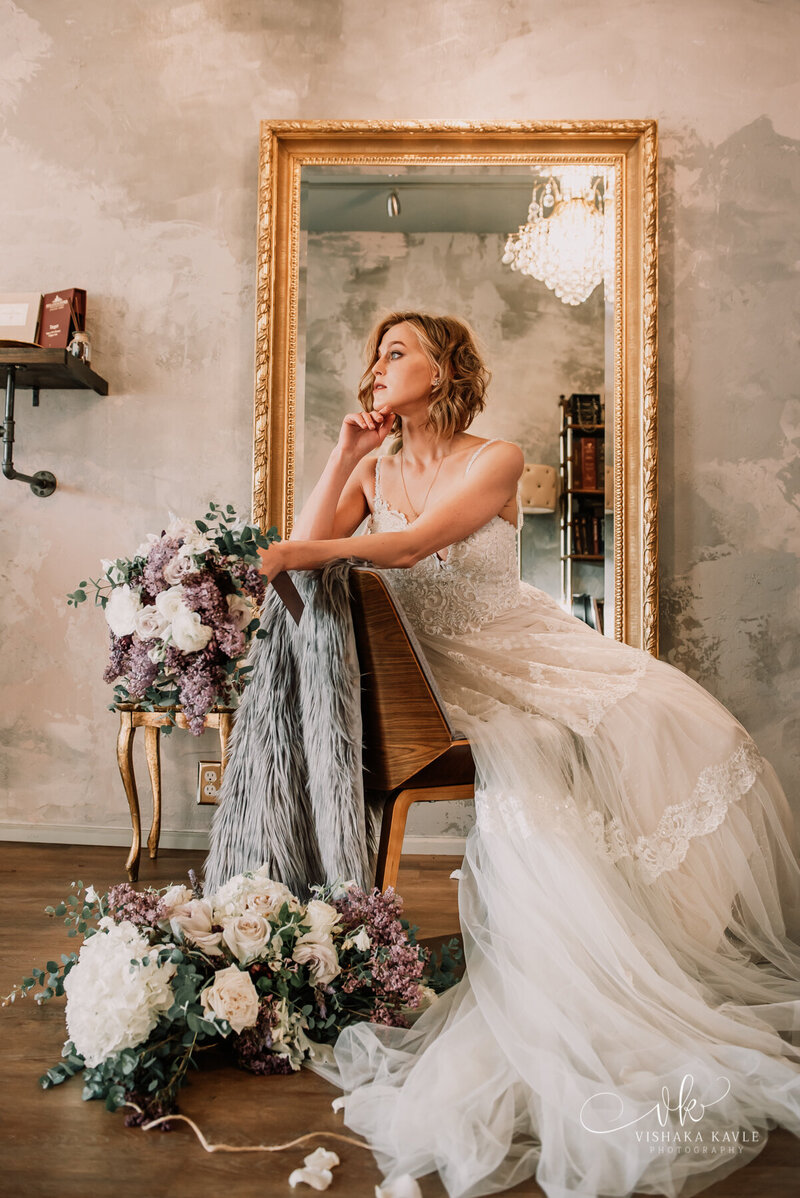 bride sitting on a chair holding her bridal bouquet with large mirror in the background