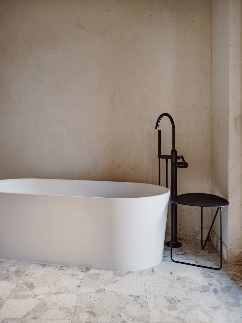 badkamer met vrijstaan bad en zwarte kraan wanden afgewerkt in betonstuc