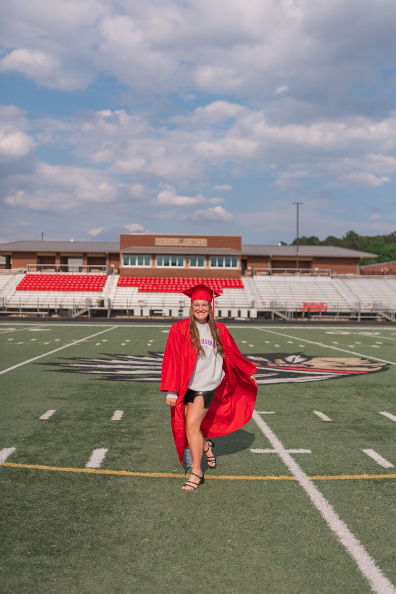 picture of high school senior in cap and gown on football field