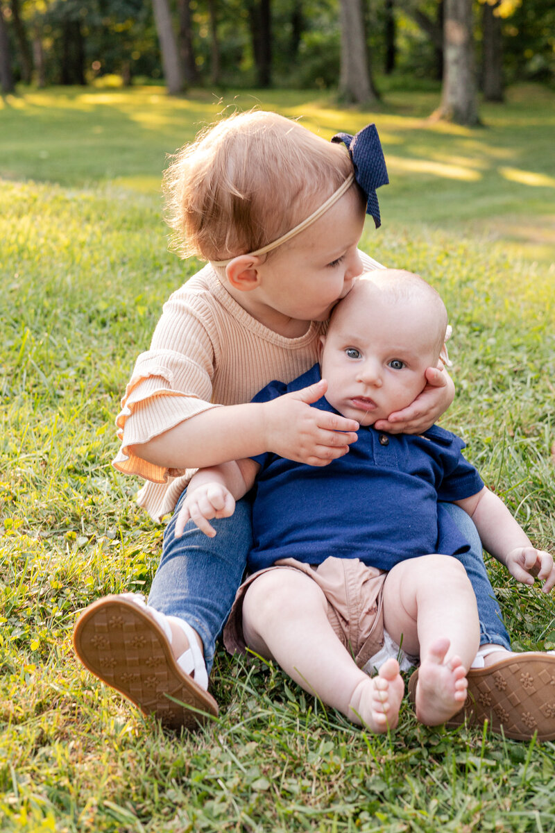 Toddler holding and kissing newborn baby brother on the head.