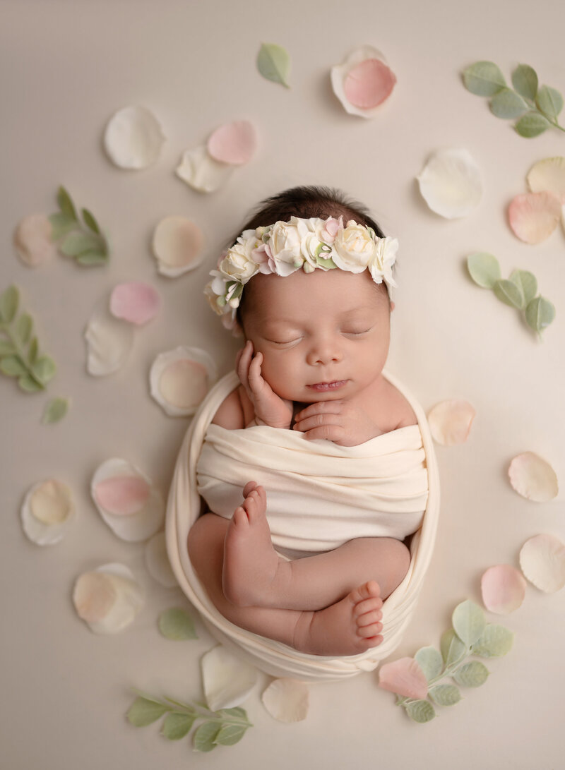 Baby girl swaddled by pastel flowers and sleeping with hand on cheek. Photo taken by Marietta photographer, Jenni Nikki Photography.
