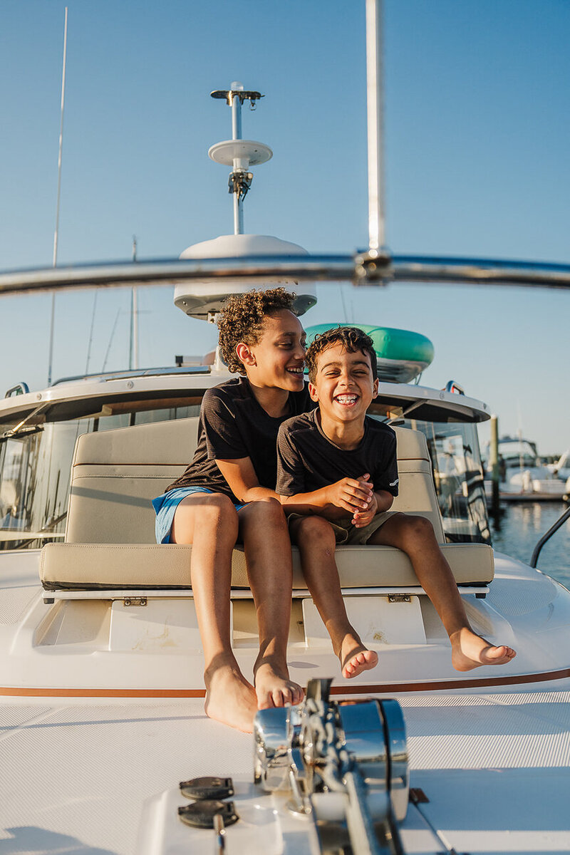 two brothers sit at the front of a boat laughing together during boston family photoshoot