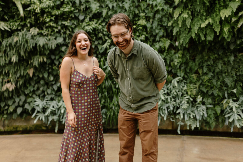 A happy couple laughs together in front of a vibrant green living wall at Longwood Gardens.