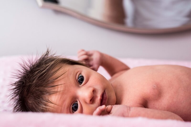 A newborn baby with a lot of hair looks at the camera for their family session