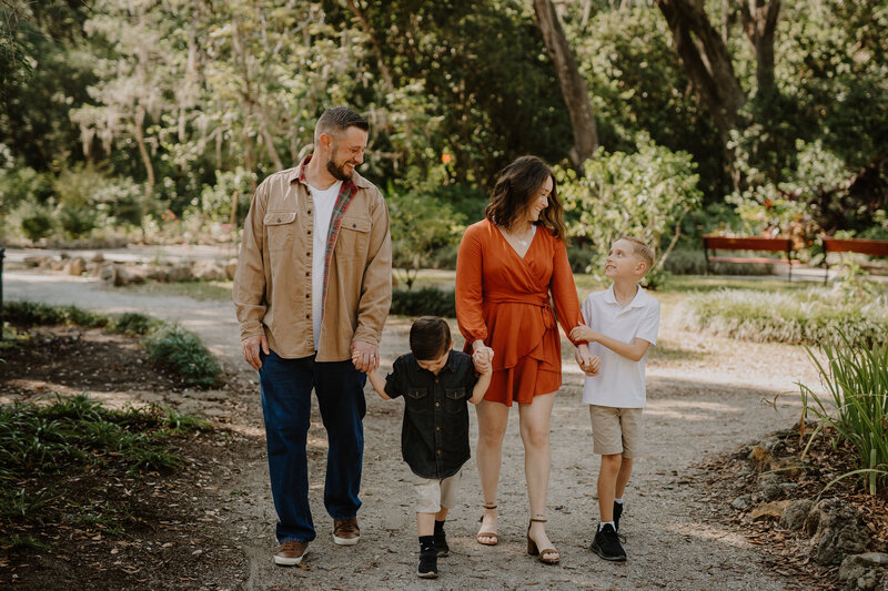 Reiki certified somatic healer and medium, Brandi of the Intuitive Momma, walks hand in hand with her two sons and husband outdoors.