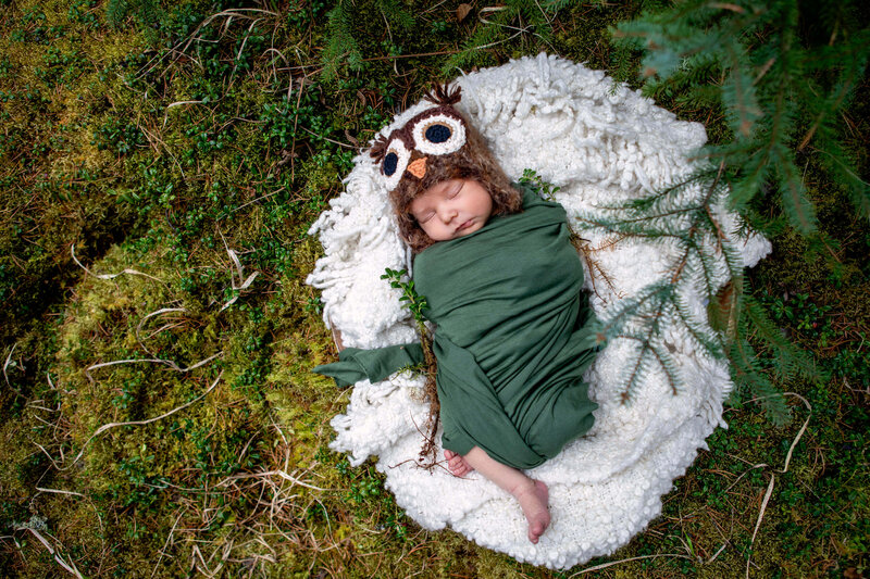 newborn boy with owl hat nestled in moss