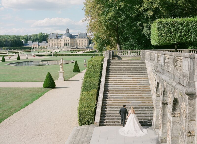 Bride and groom walking up staircase outside historic mansion in Paris