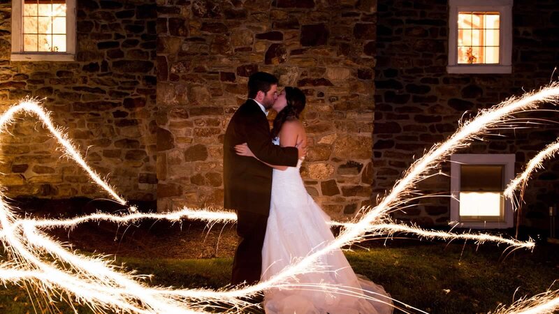 Bride & groom in front of brick wall at night surrounded by sparks