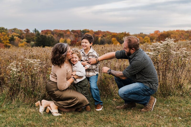 A family enjoying time together in a fall field with colorful trees in the background, captured by a family photographer Pittsburgh PA.