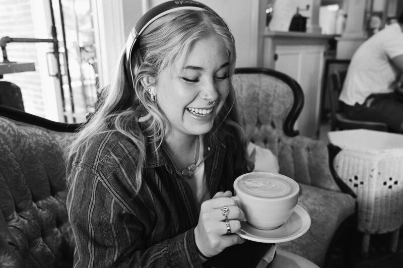 Woman smiles while holding a latte and sitting on Hillcrest Coffee's sofa