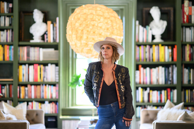 Christie Newell smiling at a bar in a stylish hat and blazer, representing her creative and approachable brand personality