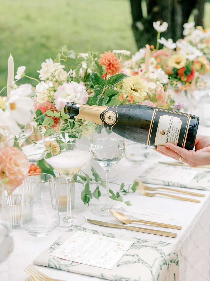 Close up of hand pouring champagne into a coupe on a wedding reception table