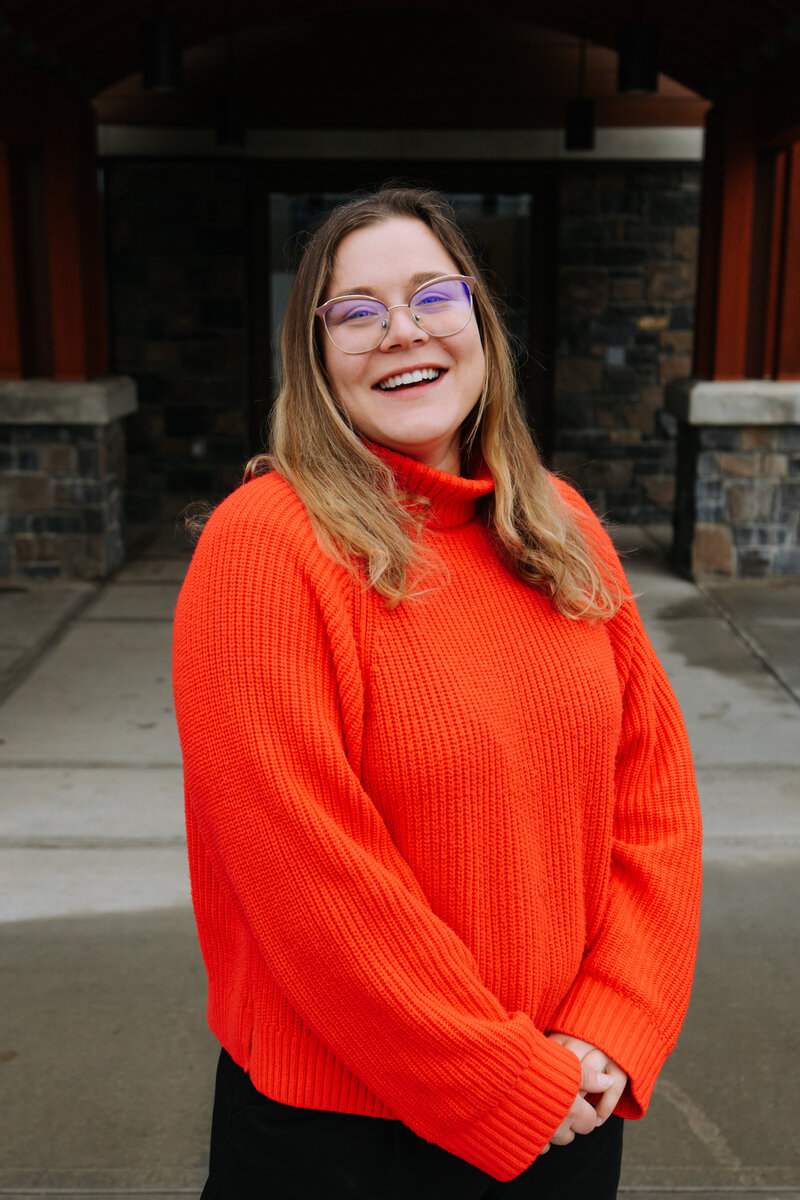 Event planner in cozy winter outfit and grey beanie smiling in snowy Banff forest – Rocky Mountain Wedding Collective