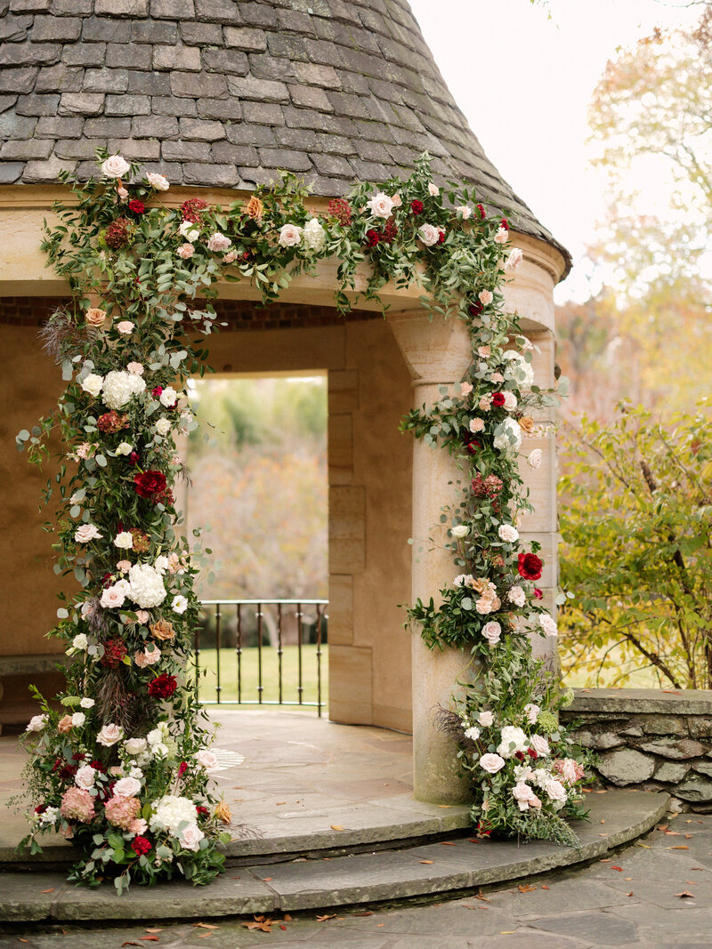 November wedding at Graylyn Estate, designed and planned by Charming Carolina — gazebo altar in the White Garden featuring a lush floral installation in blush, burgundy, and ivory tones.