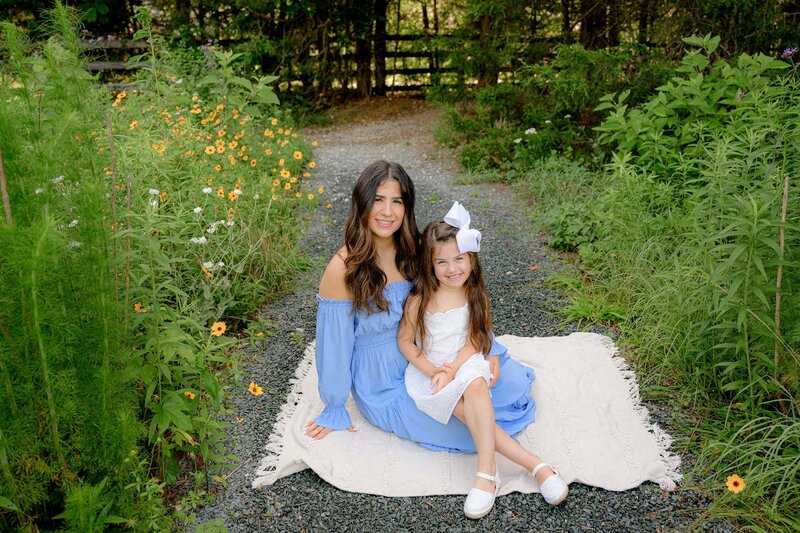 mother and daughter sit in a flower garden 
