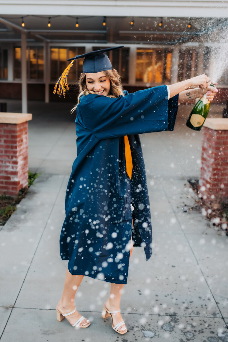Senior graduating from NAU popping a bottle of champagne by Annie Bee Photography.