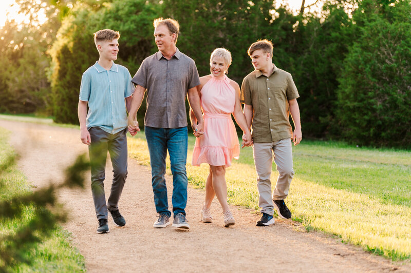 Backlit family of 4 holding hands and laughing.  Photographed by Lydia Teague Photography