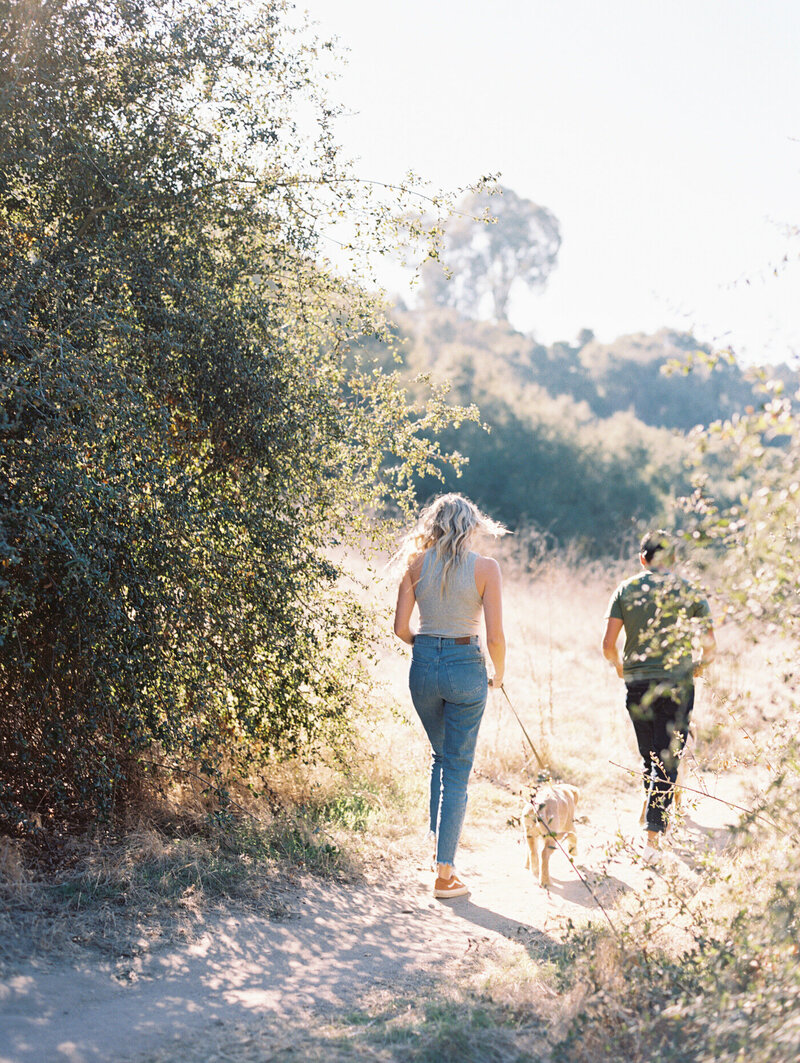 couple and their leashed golden retriever walking away