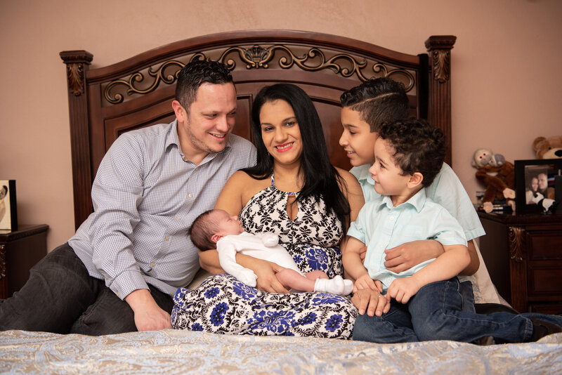 A family of 5 sitting on a bed smiling with joy and posing for their family photoshoot.