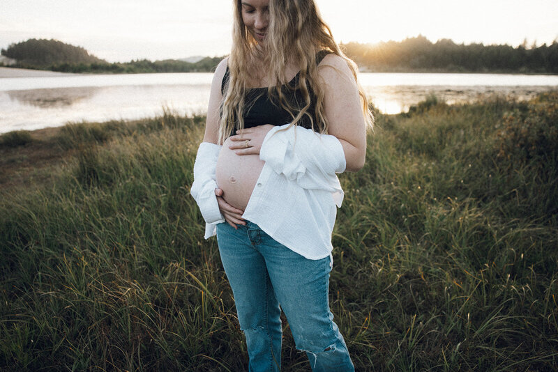Pregnant woman looks lovingly down at her belly during golden hour on the Oregon coast. 